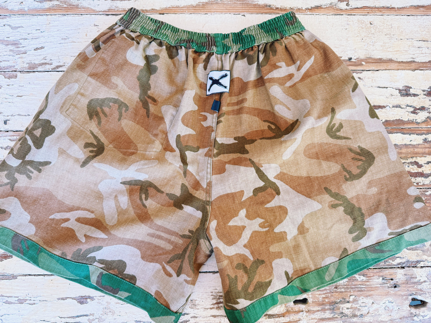 Camouflage shorts with green accents on a wooden surface