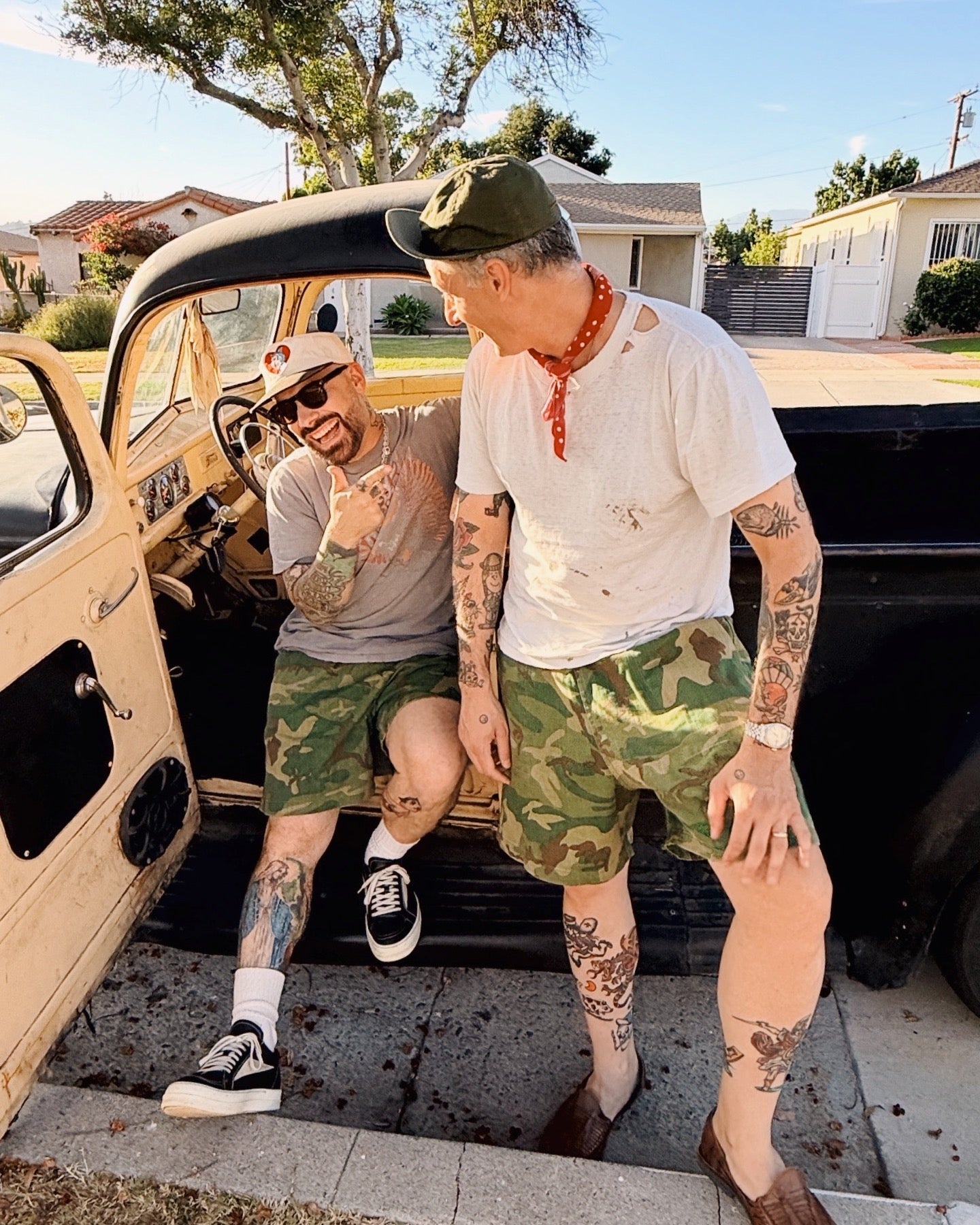 Two men standing next to a vintage car in a residential area