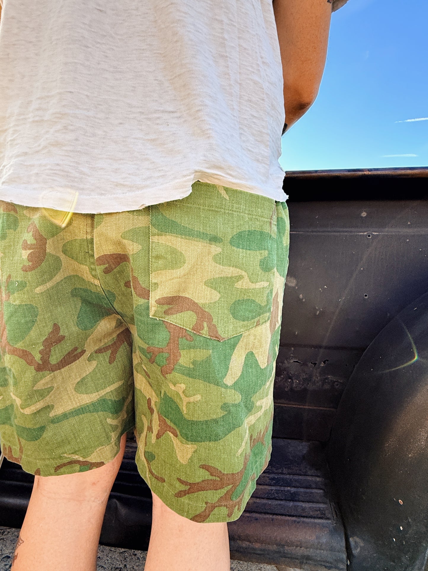 Person wearing green camouflage shorts with a white shirt, standing next to a vehicle.